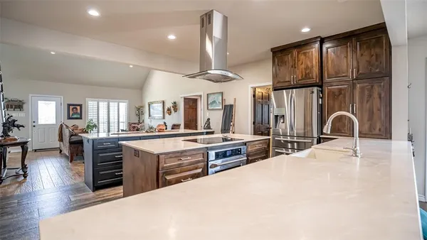 a large kitchen with stainless steel appliances kitchen island granite countertop a stove a sink a refrigerator and white cabinets with wooden floor