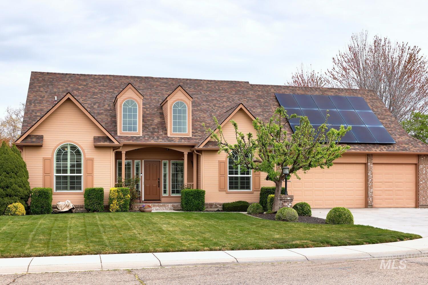 View of front facade with solar panels, roof with shingles, a front lawn, and concrete driveway