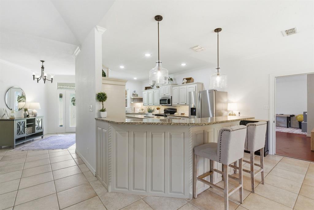 405 Zion Hill Road Weatherford, TX 76088 - Photo 11 of 38 Kitchen featuring light stone countertops, stainless steel appliances, crown molding, a kitchen bar, and white cabinetry