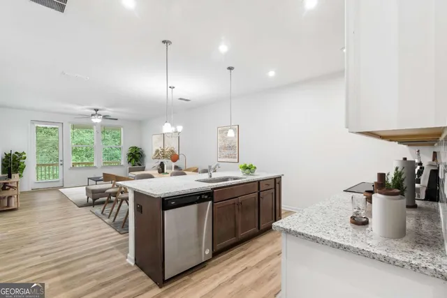 a view of a kitchen with kitchen island stainless steel appliances a sink a counter top space and wooden floor