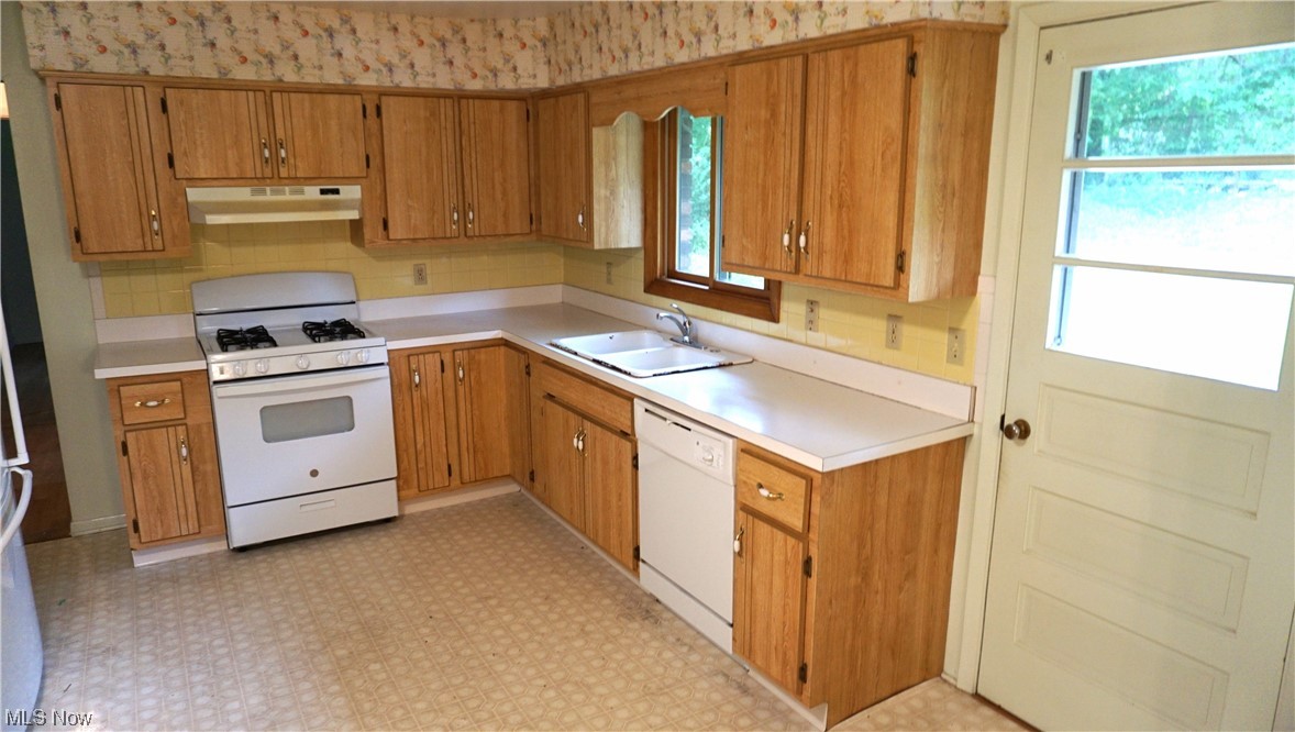 Kitchen featuring backsplash, brown cabinets, light countertops, light tile floors, and white appliances