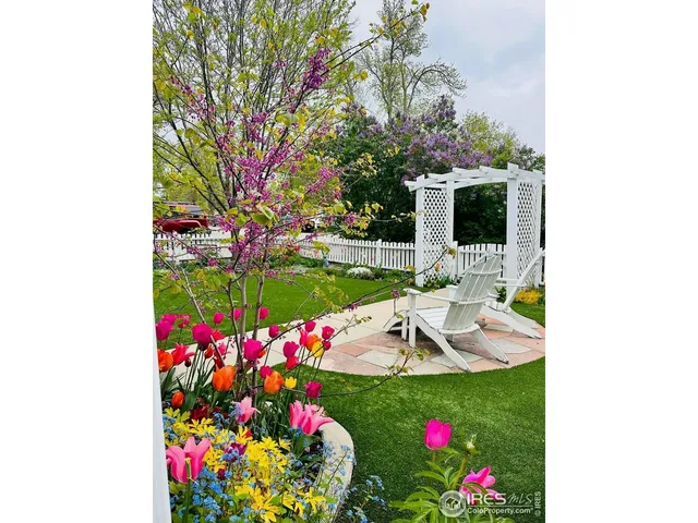 a view of a white house with a flower garden and a tree