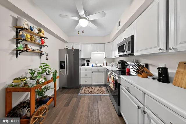 a kitchen with stainless steel appliances granite countertop a refrigerator a stove top oven a sink dishwasher and white cabinets with wooden floor