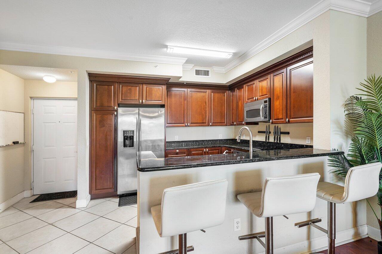 1 Renaissance Way, Unit 416 Boynton Beach, FL 33426 - Photo 7 of 31 a kitchen with granite countertop a refrigerator and wooden cabinets