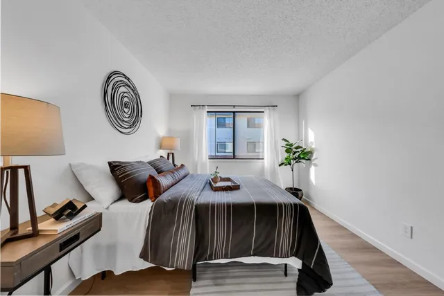 a bedroom with a bed and a lamp on table with wooden floor