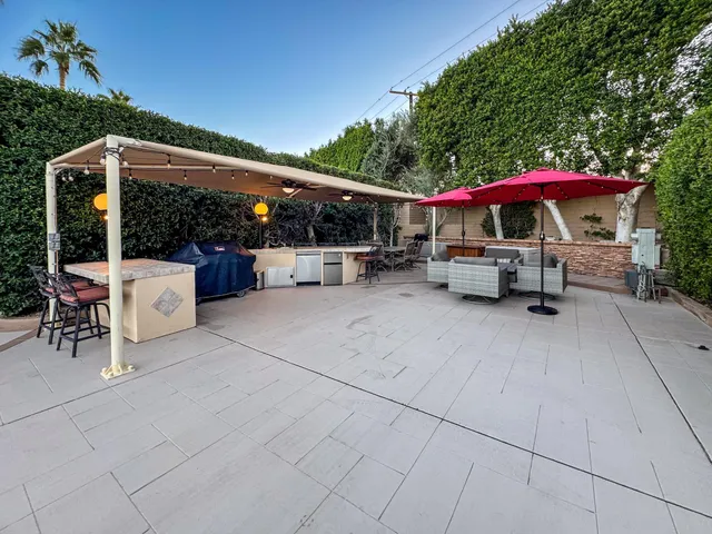 a view of a patio with table and chairs under an umbrella with a barbeque