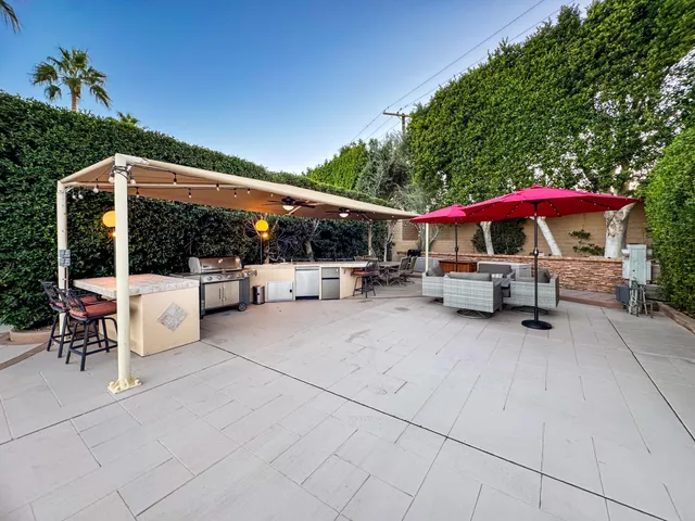 a view of a patio with a table and chairs under an umbrella with a barbeque