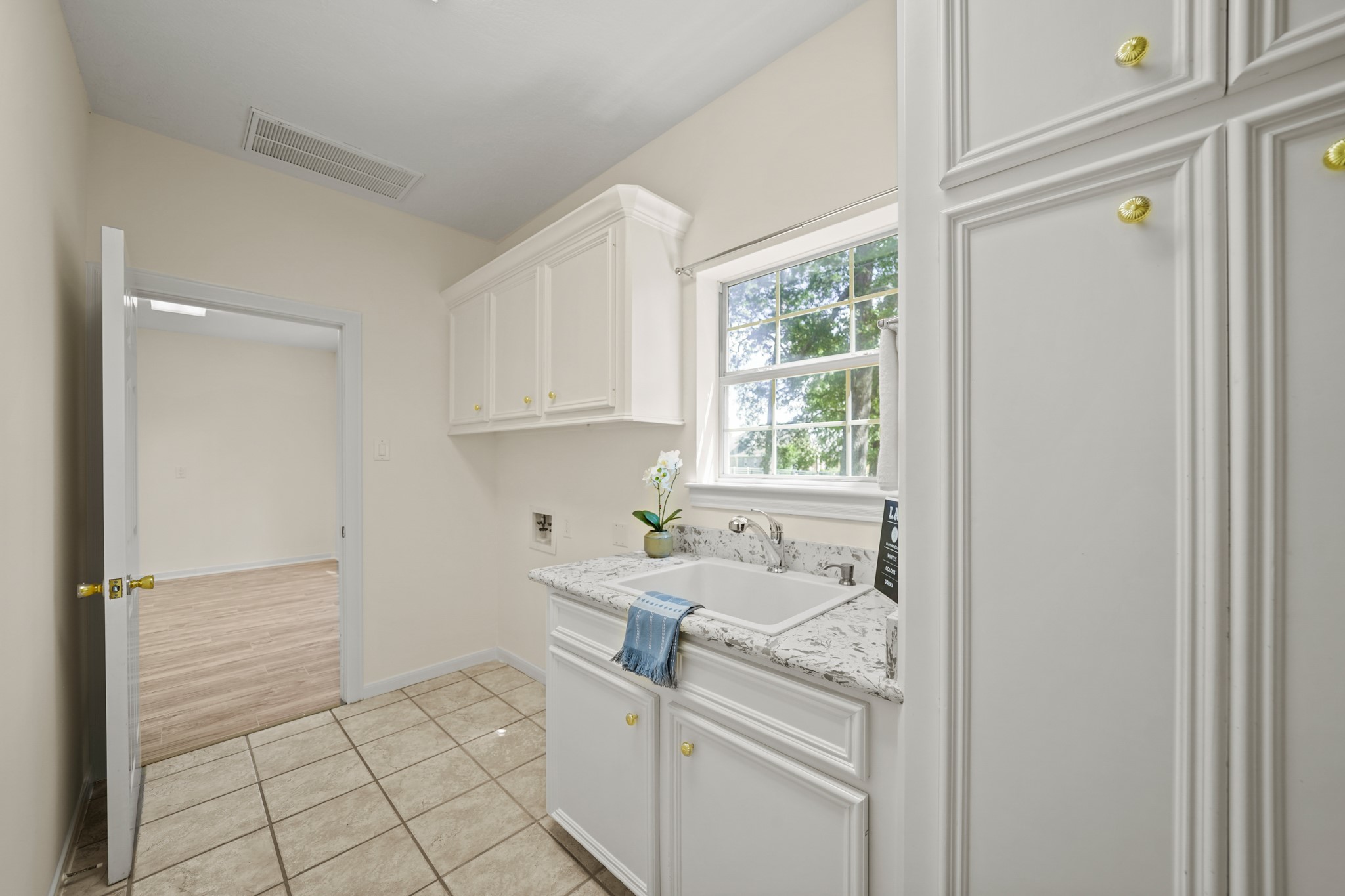 12690 Longmire Way Conroe, TX 77304 - Photo 17 of 50 Flowing seamless from the kitchen, the utility room with space for a full size washer & dryer includes upper cabinet storage, a utility sink surrounded by a granite counter top, floor-to-ceiling built storage & tile flooring. Included is a gas connection for natural gas clothes dryer and a large "bonus" room is accessible in the background.