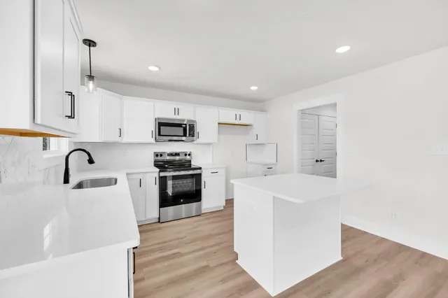 a kitchen with stainless steel appliances white cabinets a sink a stove a refrigerator and a microwave