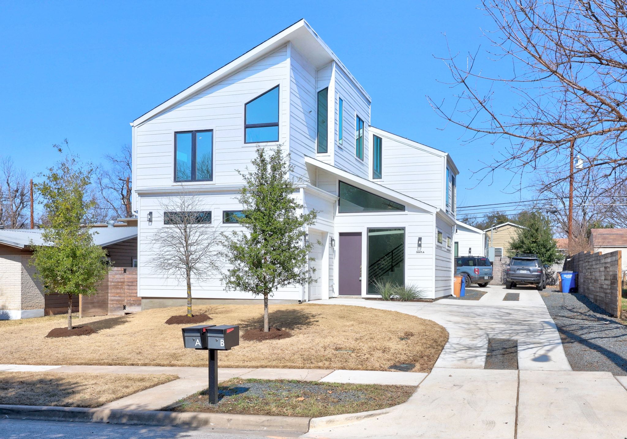 a view of a white house with a fountain plants and large tree