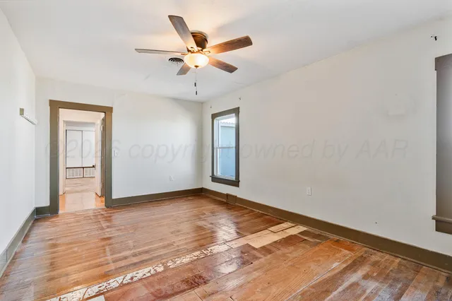 an empty room with wooden floor fan and windows