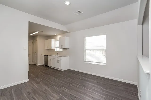 an empty room with wooden floor and a kitchen