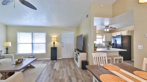 a kitchen with stainless steel appliances kitchen island granite countertop a refrigerator a sink a dining table and chairs with wooden floor