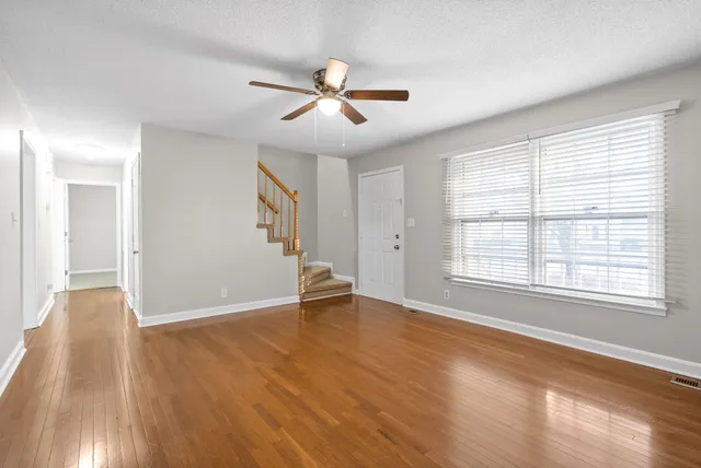 an empty room with wooden floor chandelier fan and windows