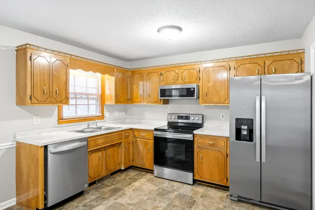 a kitchen with stainless steel appliances granite countertop a stove a sink a refrigerator white cabinets and wooden floor