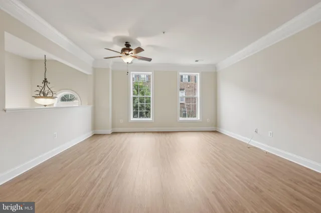 an empty room with wooden floor chandelier fan and windows
