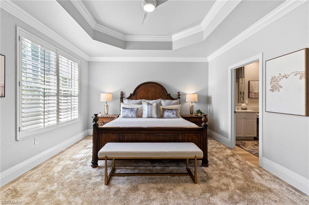 9041 Whimbrel Watch Lane, Unit 101 Naples, FL 34109 - Photo 13 of 34 Bedroom featuring ornamental molding, a tray ceiling, ensuite bath, and ceiling fan
