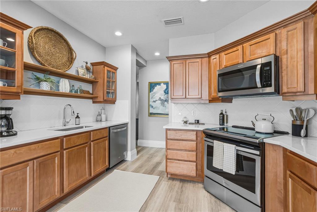9041 Whimbrel Watch Lane, Unit 101 Naples, FL 34109 - Photo 20 of 34 Kitchen featuring glass insert cabinets, stainless steel appliances, light stone counters, wood finish cabinetry, and open shelves