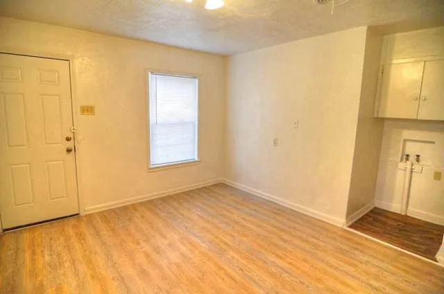 a view of an empty room with wooden floor and a window