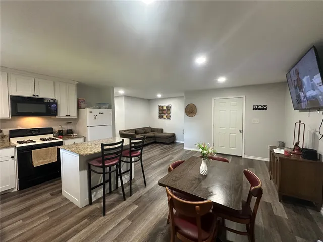 a kitchen with stainless steel appliances granite countertop a stove a refrigerator a kitchen island a table and chairs with wooden floor