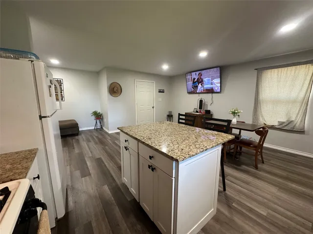 a open kitchen with stainless steel appliances granite countertop a stove a refrigerator a dining table and chairs with wooden floor