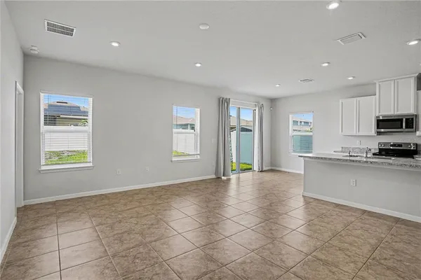 a view of an empty room with kitchen and window