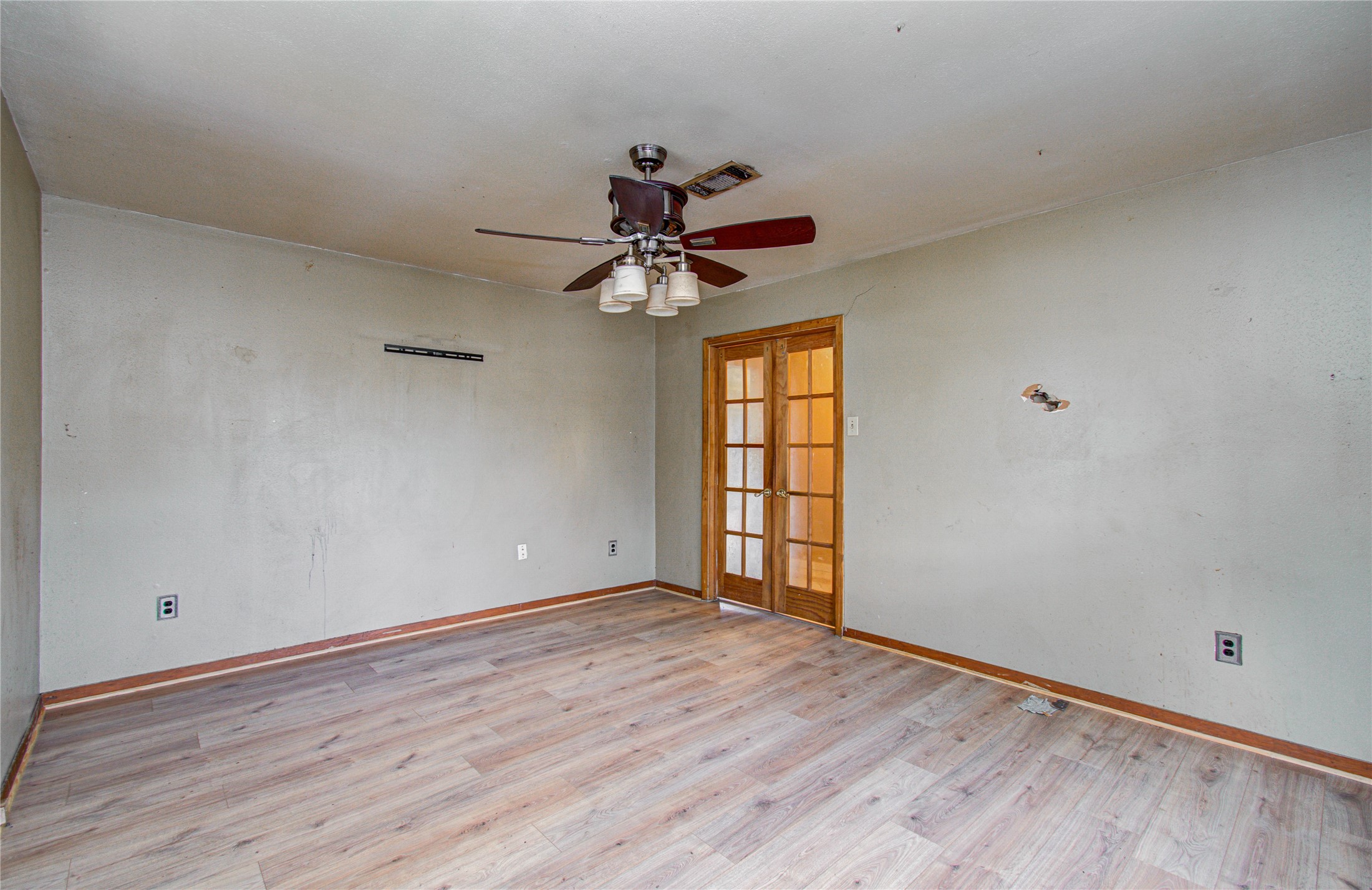 8428 Swiftwater Lane Houston, TX 77075 - Photo 5 of 26 Study room features laminate wood flooring, a ceiling fan with light fixtures, and French doors that add character. The walls show some wear, offering a great opportunity for customization and personal touches.