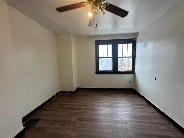 an empty room with wooden floor chandelier fan and windows