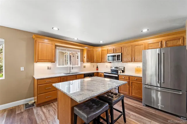 a kitchen with granite countertop a refrigerator a stove a sink dishwasher and a dining table with wooden floor