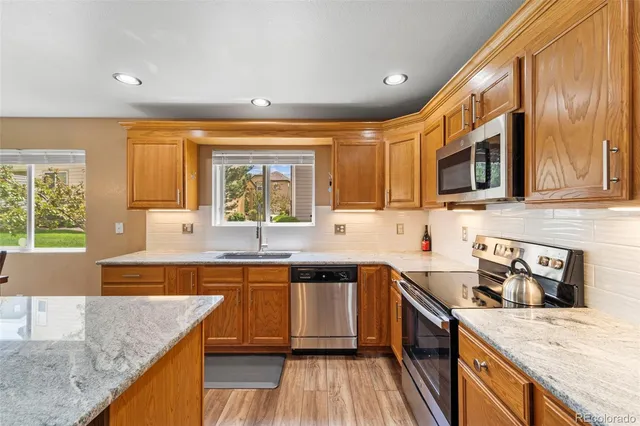 a kitchen with stainless steel appliances granite countertop wooden cabinets a sink and dishwasher a stove with wooden floor