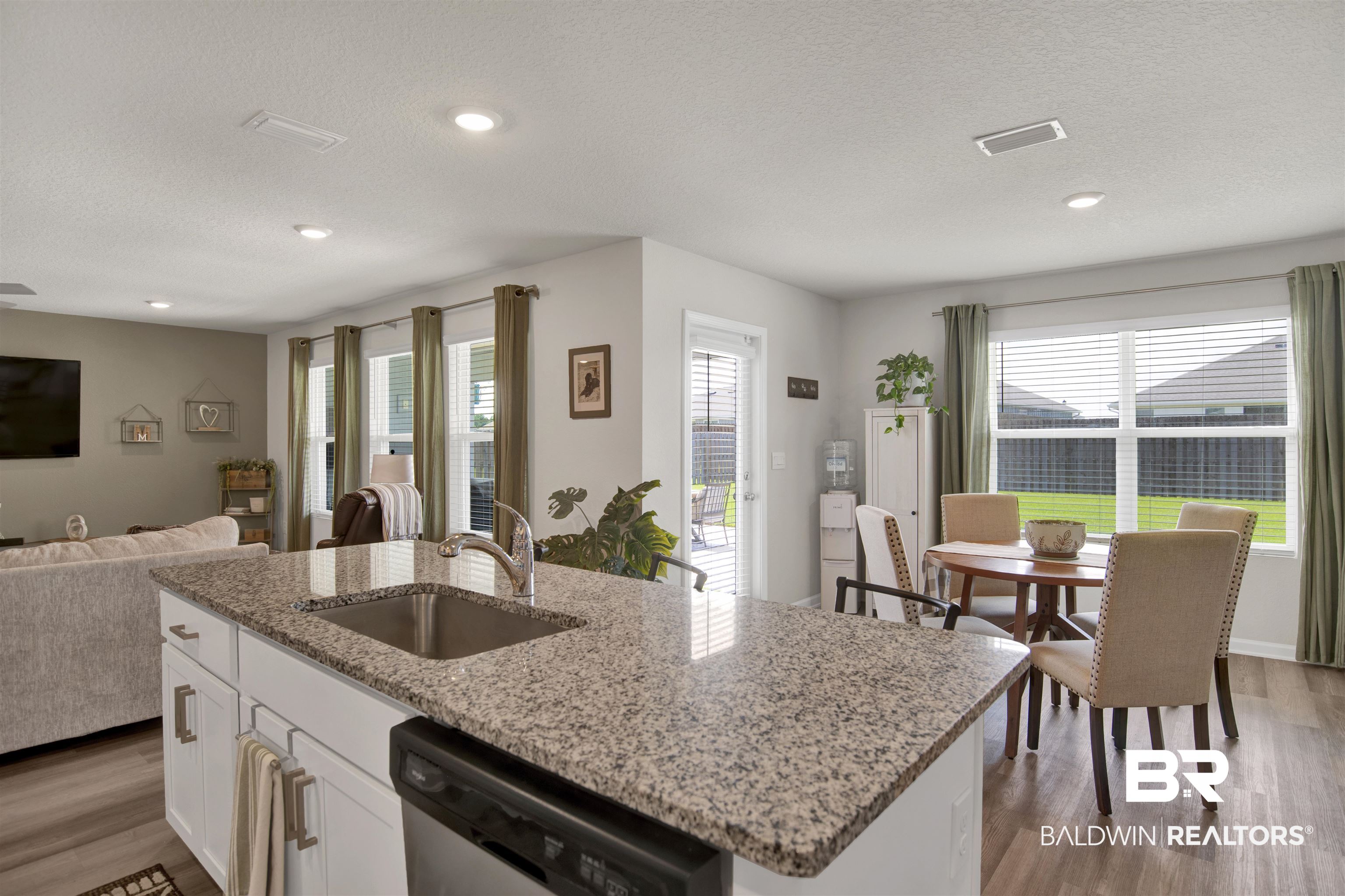 22301 Early Dawn Circle Foley, AL 36535 - Photo 30 of 45 Kitchen island featuring a stainless steel sink and granite-style countertop, white cabinetry with silver hardware, and a black dishwasher