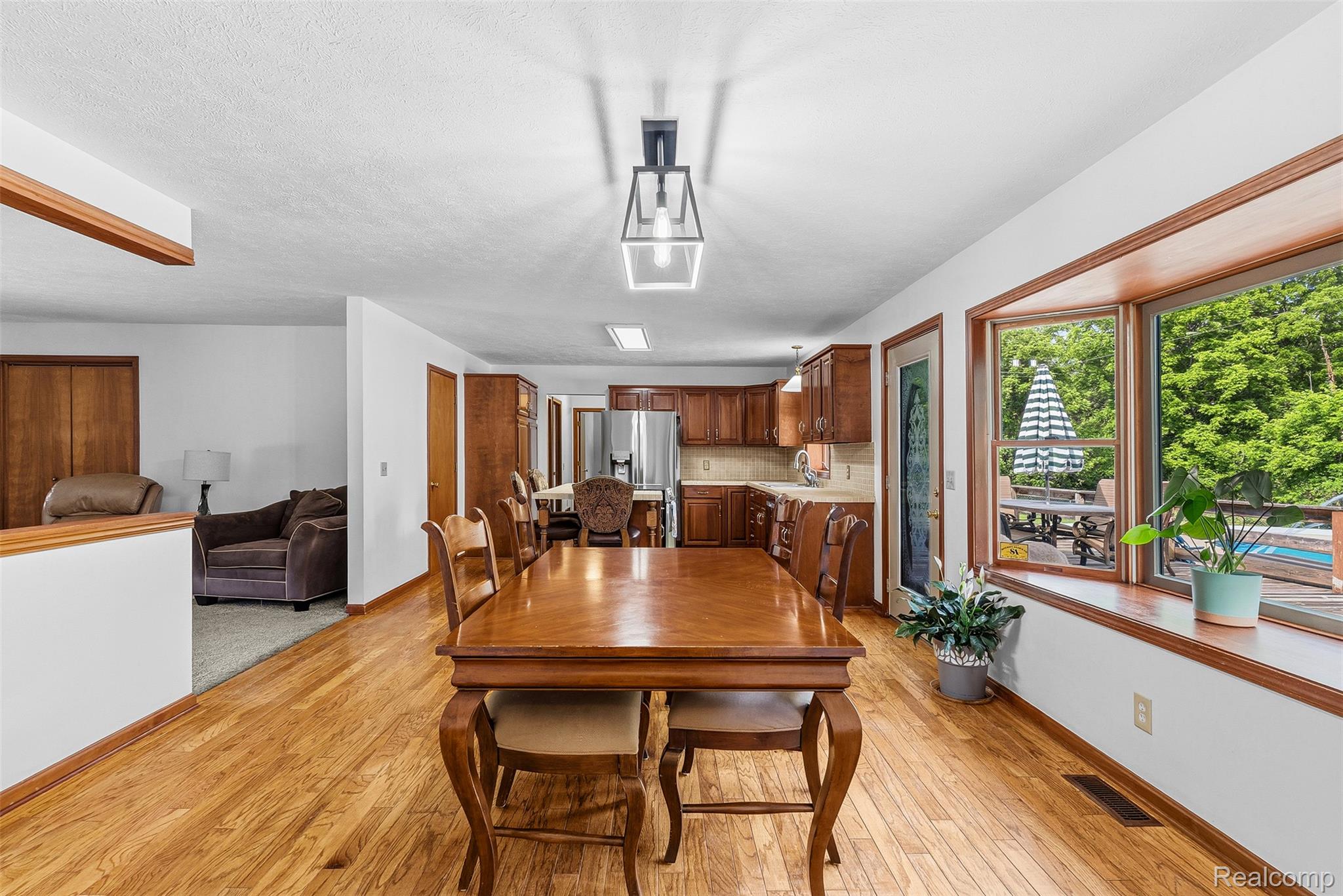 6699 Lansing Road Durand, MI 48429 - Photo 12 of 53 Open-concept dining area featuring wood-finish flooring, a contemporary linear chandelier, and a bright bay window overlooking exterior greenery