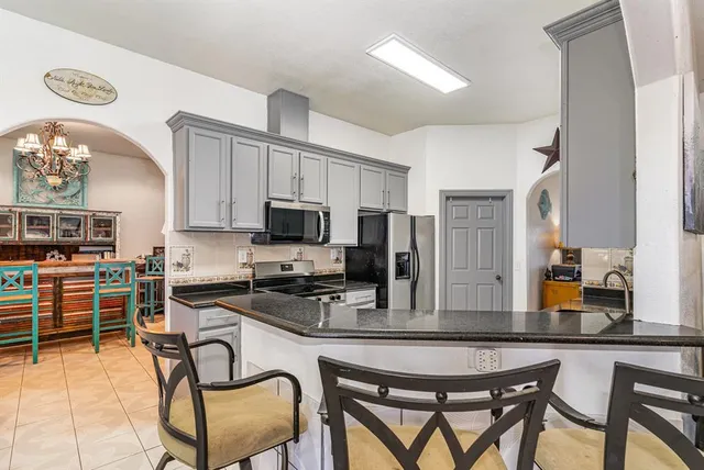 a kitchen with stainless steel appliances granite countertop a stove top oven a refrigerator a sink a dining table and chairs with wooden floor