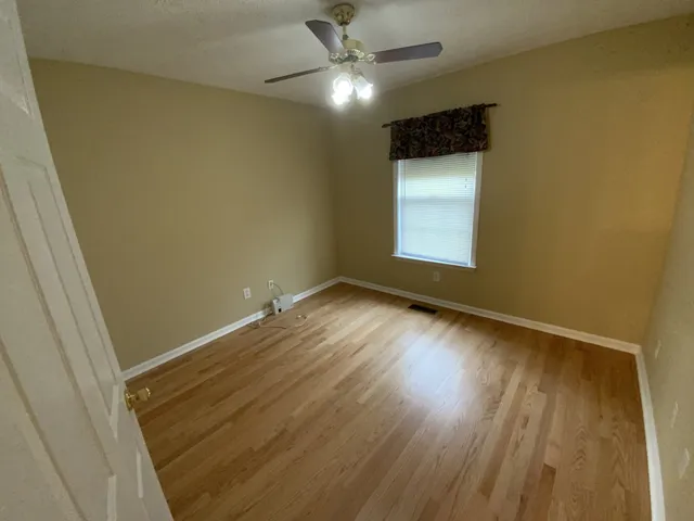 a view of an empty room with wooden floor and a fan