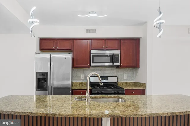 a kitchen with stainless steel appliances granite countertop a refrigerator a stove and a sink with wooden floor