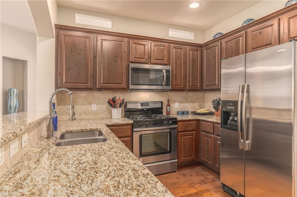 6708 Menchaca Road, Unit 14 Austin, TX 78745 - Photo 12 of 22 Kitchen featuring granite countertops, stainless steel appliances, wood-finish flooring, full-height cabinetry, and a tile backsplash