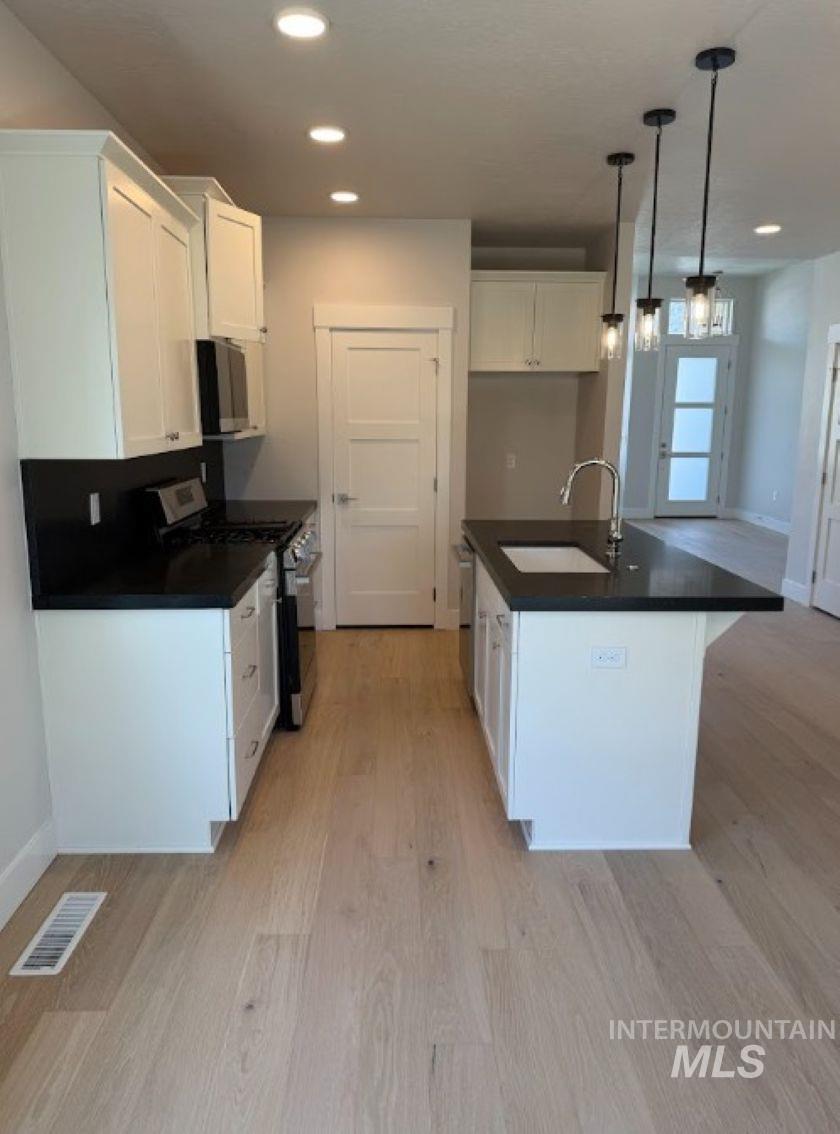 665 West Wrangler Street Meridian, ID 83646 - Photo 3 of 18 Bright kitchen featuring white shaker cabinetry, dark countertops, a central island with an undermount sink, pendant lighting, and wood-finish flooring