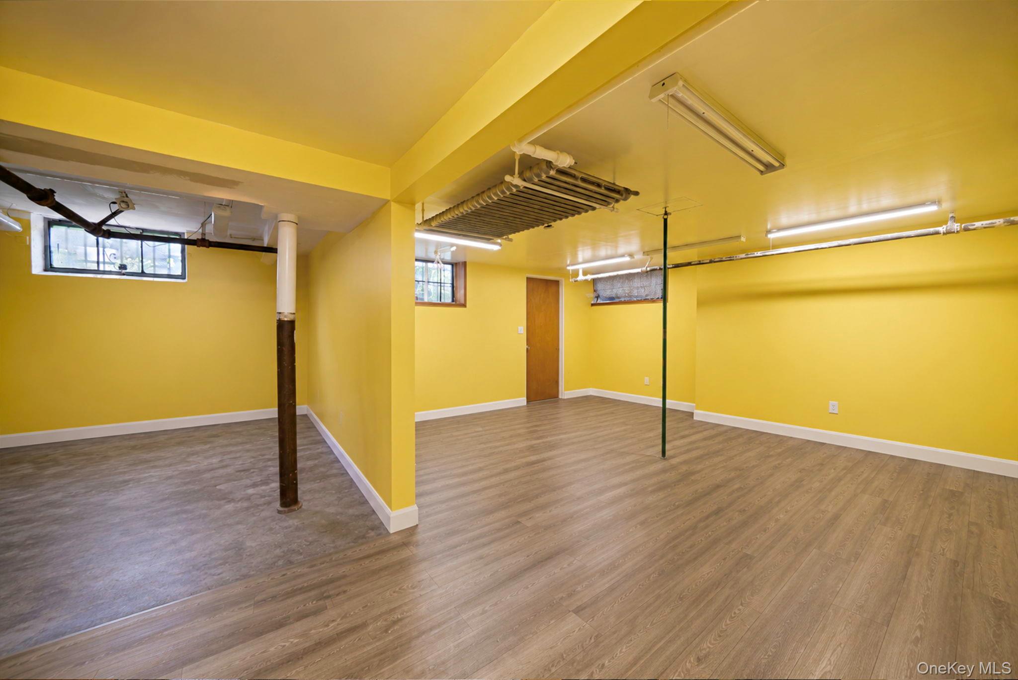 18240 Avon Road Queens, NY 11432 - Photo 27 of 30 Lower level featuring wood-finish flooring, bright yellow walls, white trim, and multiple fluorescent lighting fixtures