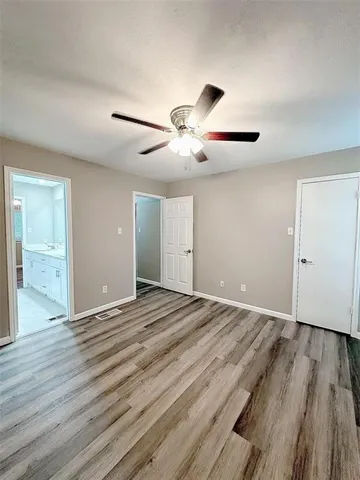 a view of an empty room with wooden floor and a ceiling fan