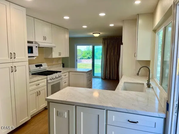a kitchen with kitchen island granite countertop a stove a sink a refrigerator and white cabinets with wooden floor