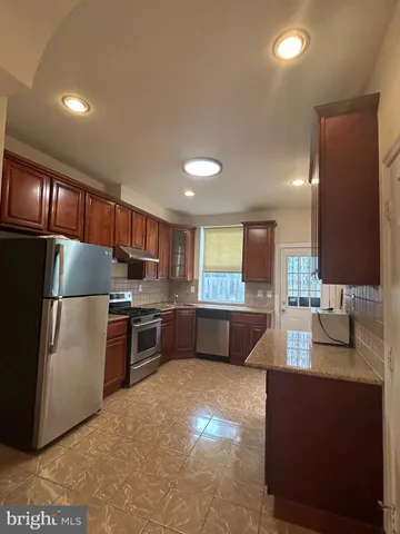 a large kitchen with stainless steel appliances kitchen island granite countertop a refrigerator a stove a sink and a dining table with wooden cabinet