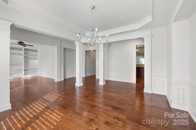 an empty room with wooden floor chandelier and windows