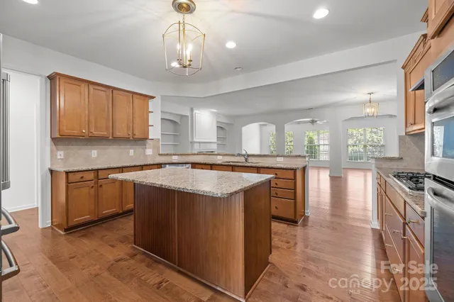 a kitchen with stainless steel appliances granite countertop a stove top oven a sink dishwasher a dining table and chairs with wooden floor