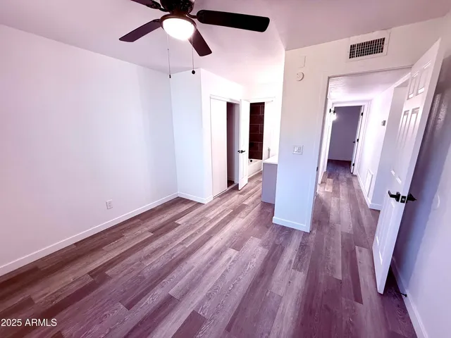 a view of an empty room with wooden floor and a ceiling fan