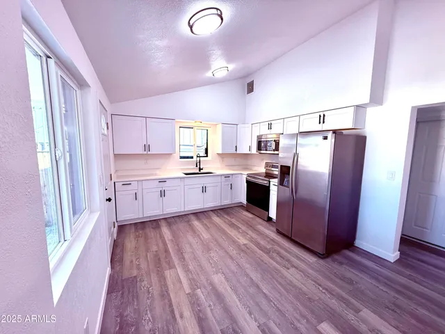 a kitchen with stainless steel appliances granite countertop a refrigerator a sink dishwasher a stove and white countertops with wooden floor