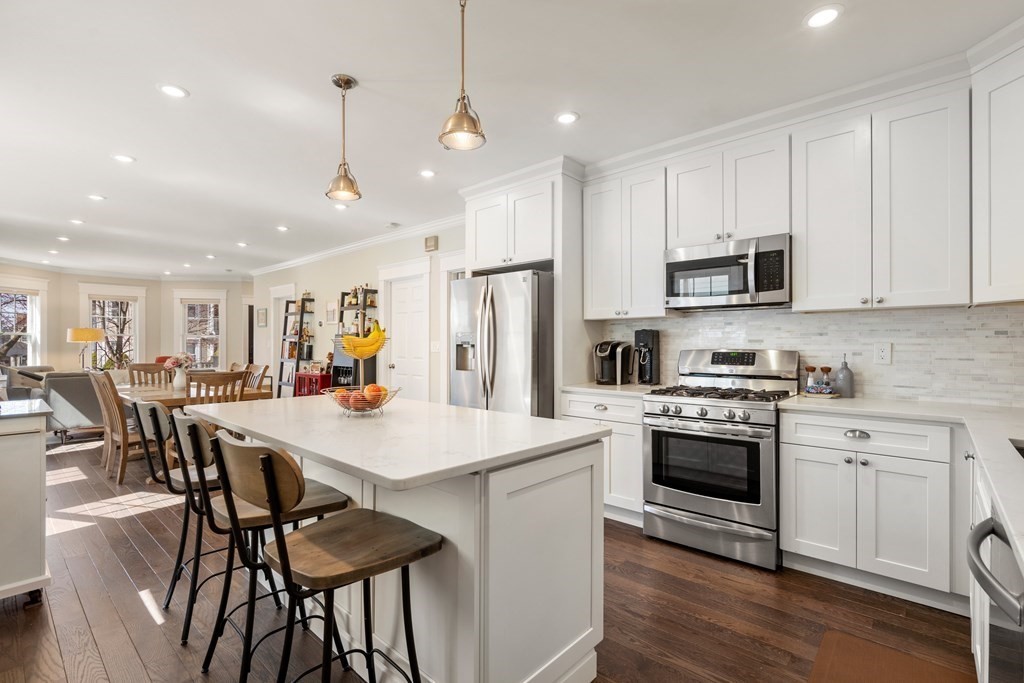 a kitchen with stainless steel appliances granite countertop a stove a refrigerator a kitchen island a stove a table and chairs with wooden floor