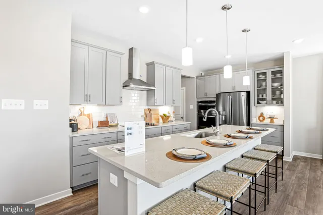 a kitchen with stainless steel appliances kitchen island granite countertop a sink a stove a refrigerator and white cabinets with wooden floor