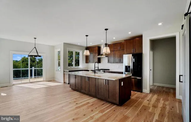 a kitchen with stainless steel appliances a stove top oven a sink dishwasher a refrigerator and a oven with wooden floor