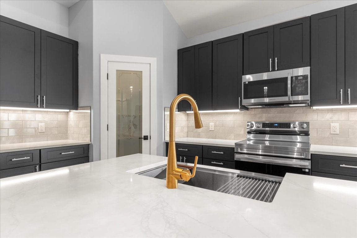 217 Gato Road Cedar Creek, TX 78612 - Photo 11 of 39 Kitchen with appliances with stainless steel finishes, dark cabinets, light stone counters, and backsplash