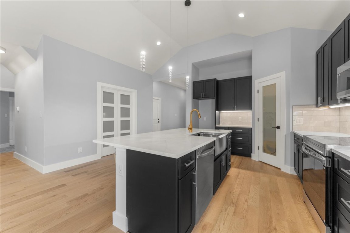217 Gato Road Cedar Creek, TX 78612 - Photo 12 of 39 Kitchen with vaulted ceiling, dark cabinets, decorative backsplash, stainless steel appliances, and an island with sink